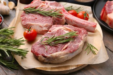 Çiğ et parçaları, biberiye ve domatesler ahşap masada, yakın plan.