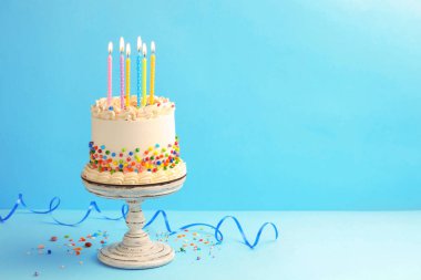 Renkli şekerli nefis bento keki, yanan mumlar ve beyaz masada serpentin şerit. Metin için boşluk