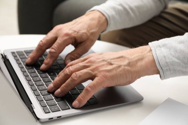 Masada dizüstü bilgisayar kullanan kıdemli bir adam, yakın plan.