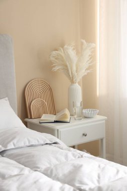 Yatağın yanında kitap, dekor ve bir bardak su olan komodin.