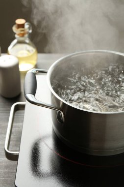 Kaynar suyla pişirme tenceresi ve ahşap masa üzerinde gri arka plan, yakın çekim
