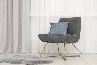 Açık gri pencere perdesi ve modern koltuk.