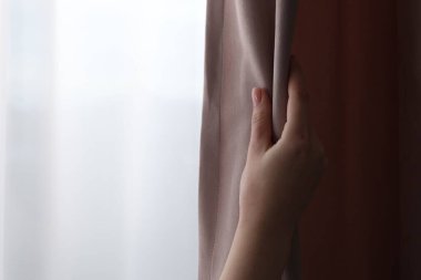 Woman opening stylish curtains at home, closeup. Space for text