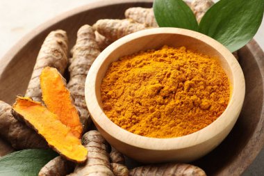 Kasede Aromatik zerdeçal tozu, taze kökler ve açık gri masadaki yapraklar, yakın plan.