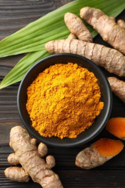 Akvaryumdaki Aromatik zerdeçal tozu, taze kökler ve ahşap masa üzerindeki yapraklar, düz uzanmış.