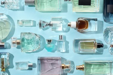 Bottles of various perfumes on light blue background, flat lay