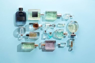 Bottles of various perfumes on light blue background, flat lay