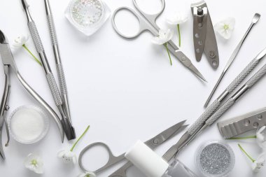 Beyaz arka planda farklı manikür aletleri ve çiçeklerden oluşan bir çerçeve. Metin için boşluk