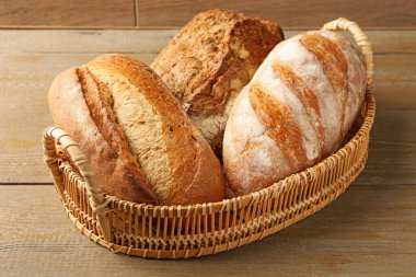 Hasır sepetin içinde farklı türde taze ekmek, ahşap masada, yakın plan.