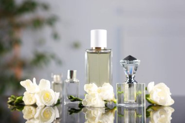 Ayna yüzeyinde aromatik parfüm şişeleri ve çiçekler bulanık arka planda, yakın plan
