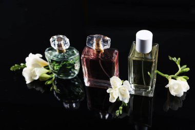 Siyah ayna yüzeyinde aromatik parfüm şişeleri ve çiçekler
