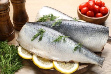 Ahşap masada dereotu ve limon dilimli lezzetli ringa filetoları, yakın plan.