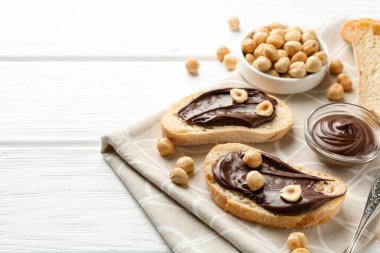 Çikolata sürülmüş ekmek dilimleri ve beyaz ahşap masada fındıklar, yakın plan. Metin için boşluk