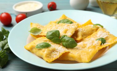 Açık mavi ahşap masada servis edilen peynirli ve fesleğenli lezzetli ravioli.