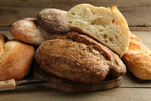 Tahta masada farklı somun taze ekmek ve bıçak, yakın plan.