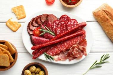 Farklı tütsülenmiş sosisler beyaz ahşap masada servis edilir.