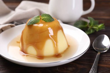 Karamel soslu lezzetli puding ve ahşap masada servis edilen nane, yakın plan.