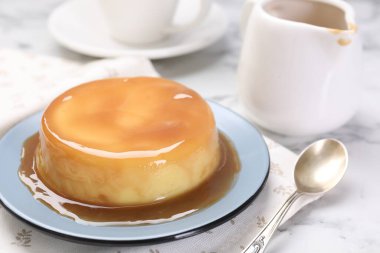 Karamel soslu lezzetli puding ve beyaz mermer masada kaşık, yakın plan.