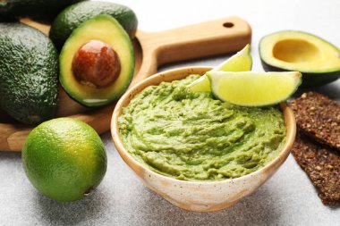 Lezzetli avokado sosu, limon ve gevrekler açık gri masada, yakın plan.