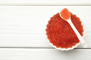 Lezzetli kırmızı havyar kasede ve kaşıkla beyaz ahşap masa, üst manzara. Metin için boşluk