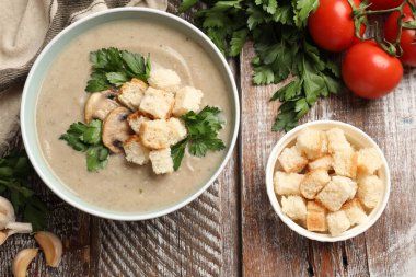 Lezzetli mantar kremalı çorba, kızarmış ekmek ve ahşap masadaki malzemeler.