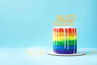 Lezzetli gökkuşağı doğum günü pastası ve açık mavi arka planda konfeti, metin için yer