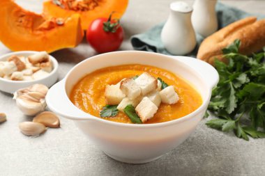 Lezzetli balkabağı kremalı çorba, kıtır ekmekli ve maydanozlu, gri desenli masa, yakın plan.