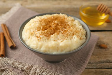 Tarçınlı lezzetli sütlaç, bal ve badem ahşap masada, yakın plan.