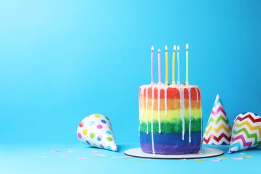 Lezzetli gökkuşağı pastası yanan mumlar, parti şapkaları ve açık mavi arka planda konfeti, mesaj için yer