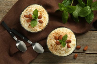 Tarçınlı lezzetli sütlaç, badem ve nane şekeri ahşap masada servis edilir.