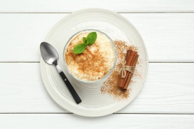 Tarçınlı leziz pirinç pudingi, beyaz ahşap masada nane ve kaşık, üst manzara.