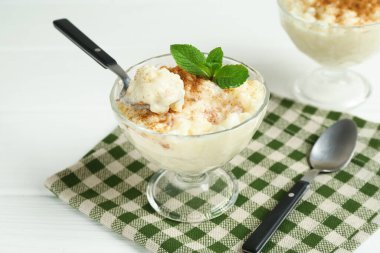 Tarçınlı lezzetli sütlaç, nane ve kaşıklar beyaz ahşap masada, yakın plan.