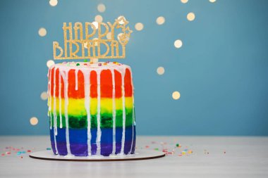 Açık mavi arkaplanlı, bulanık ışıklı, beyaz masadaki tepeli nefis gökkuşağı doğum günü pastası, yakın plan. Metin için boşluk