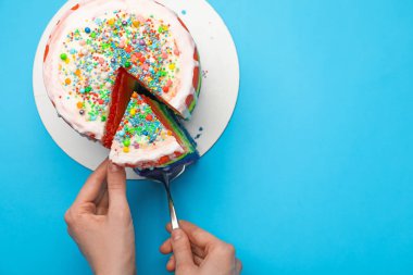 Açık mavi masada spatulayla lezzetli bir gökkuşağı pastası yiyen bir kadın. Metin için boşluk