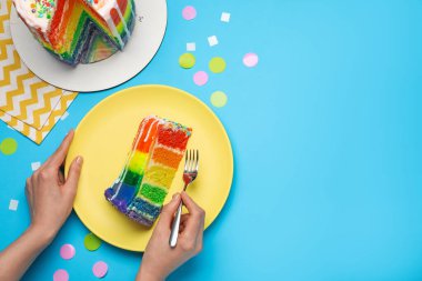 Açık mavi masada konfetiyle lezzetli gökkuşağı pastası yiyen bir kadın. Metin için boşluk