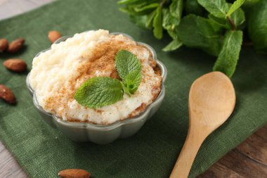 Tarçınlı, naneli, bademli ve ahşap masadaki kaşıklı lezzetli sütlaç.