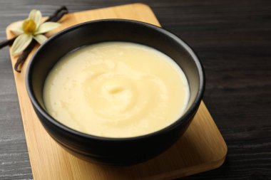 Lezzetli vanilyalı puding kasede, çiçek ve kapsüller ahşap masada, yakın plan