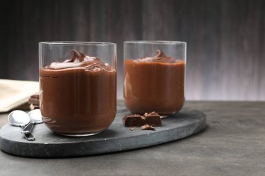 Lezzetli puding ve çikolata parçaları gri masada, yakın plan.