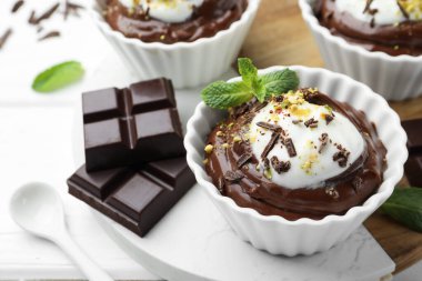 Krem şantili lezzetli puding ve beyaz ahşap masadaki çikolata parçaları, yakın plan.