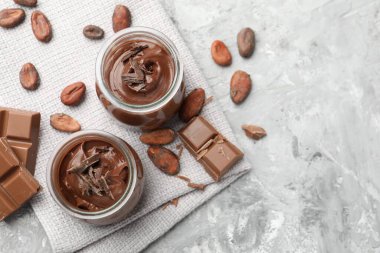 Cam kavanozlarda lezzetli puding, çikolata parçaları ve açık gri masada kakao çekirdeği, düz yatak. Metin için boşluk