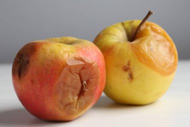 Beyaz ahşap masa üzerinde çürük elmalar Gri arka plan karşı, yakın plan