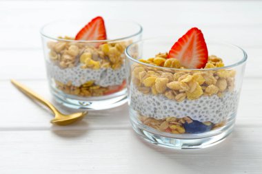 Chia tohumlu lezzetli tatlı, yoğurt, granola ve beyaz ahşap masadaki bardaklarda çilek, yakın plan. Süper yemek.