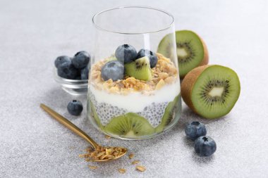 Chia tohumlu lezzetli tatlı, yoğurt, granola, yaban mersini ve kivi açık gri masada, yakın plan. Süper yemek.