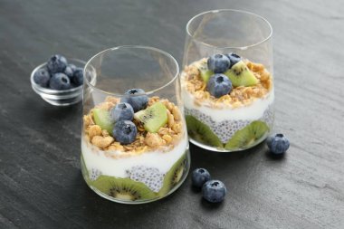 Chia tohumlu lezzetli tatlı, yoğurt, granola, yaban mersini ve kivi gri masada, yakın plan. Süper yemek.