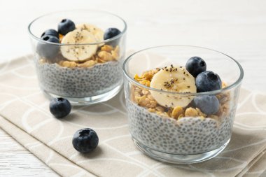 Chia tohumlu lezzetli tatlı, yoğurt, granola, yaban mersini ve muz beyaz ahşap masada, yakın plan. Süper yemek.