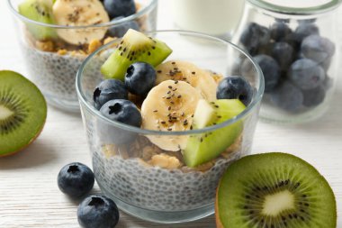 Chia tohumlu lezzetli tatlı, yoğurt, granola, yaban mersini, muz ve kivi beyaz ahşap masada, yakın plan. Süper yemek.