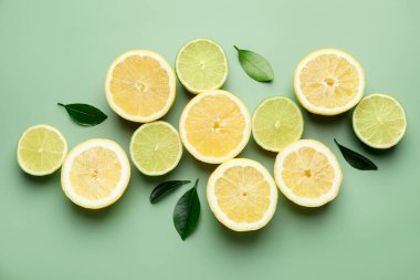 Soluk yeşil arka planda limon ve limon dilimleri, düz uzanmış.