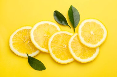 Sarı arka planda taze limon ve yeşil yapraklar var.