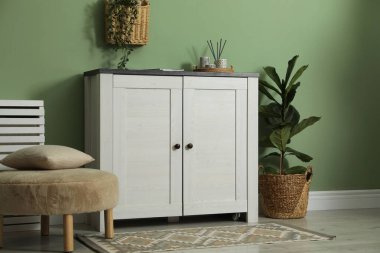 Farklı dekorlu bir dolap ve yeşil duvarın yanında pouf. İç tasarım