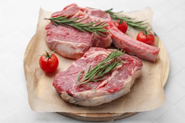 Çiğ et parçaları, biberiye ve domatesler beyaz fayanslı masada, yakın plan.